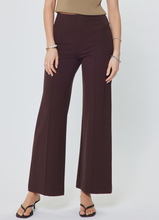 Load image into Gallery viewer, A model wearing high-waisted, wide-leg cropped pants in a deep plum or eggplant shade, paired with a beige top and black heeled sandals, against a light gray studio background.

