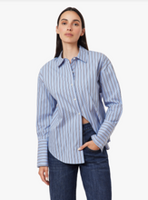 Load image into Gallery viewer, A woman modeling a light blue and white vertically striped button-down shirt with dark blue jeans, set against a plain light gray background.
