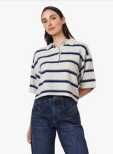 Load image into Gallery viewer, A woman modeling a short-sleeve knit polo shirt with horizontal navy and grey stripes, paired with dark blue jeans, against a plain light gray background.
