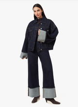 Load image into Gallery viewer, A model wearing a dark indigo denim jacket and matching wide-leg jeans with contrasting light gray cuffed details, paired with dark brown heeled boots, against a plain white studio background.
